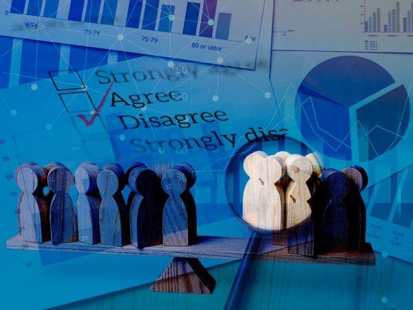 εικόνα που δείχνει ξύλινες φιγούρες σε σχήμα ανθρώπου να βρίσκονται σε ζυγαριά και πίσω στοιχεία από δημοσικοπήσεις και ένα τικ στη λέξη «Διαφωνώ»