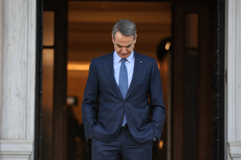 εικόνα που δείχνει τον Κυριάκο Μητσοτάκη με σκυφτό το κεφάλι να αναμένει Ευρωπαία αξιωματούχο στην είσοδο του Μεγάρου Μαξίμου