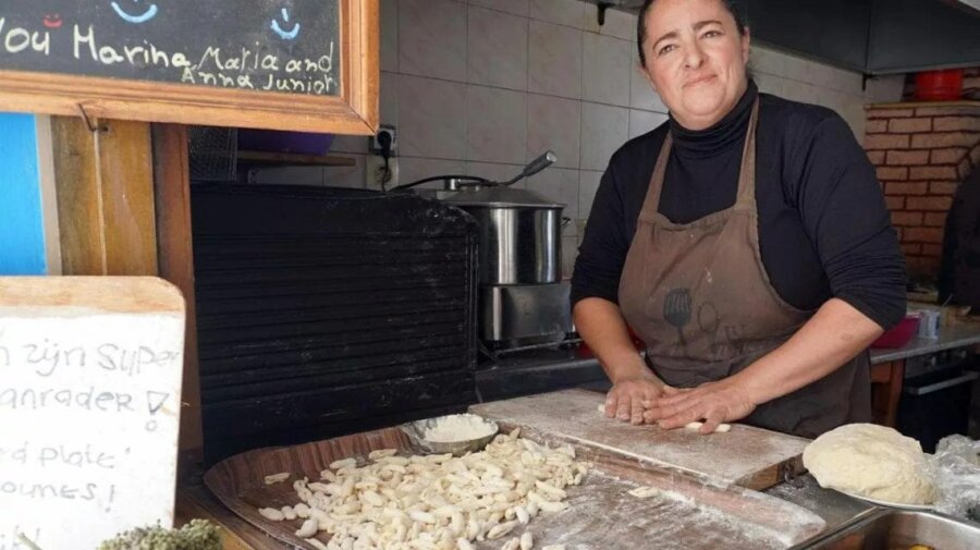 εικόνα που δείχνει τη Μαρία Κανάκη να ζυμώνει τις μακαρούνες μπροστά στο παράθυρο της μικρής ταβέρνας της στην Κάρπαθο