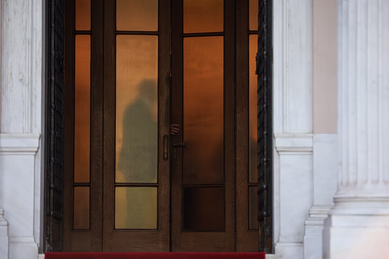Εικόνα που δείχνει φιγούρες πίσω από την πόρτα εισόδου στο Μέγαρο Μαξίμου